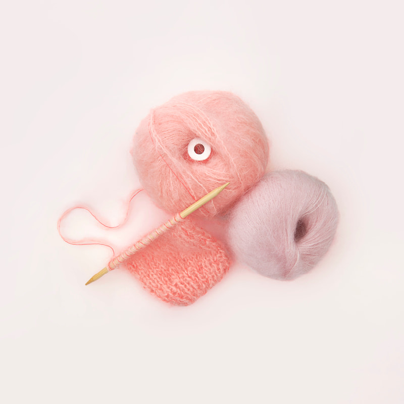 Ein Strickstück auf einer Stricknadel und Wollknäuel liegen auf grauem Hintergrund. 