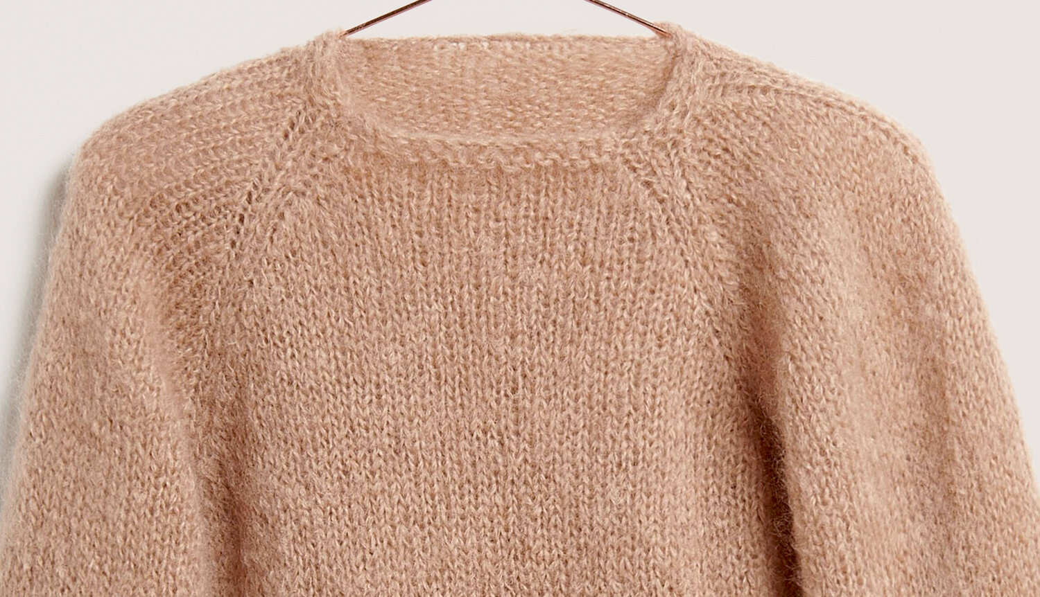 Strickanleitung Pullover aus Fashion Mohair Merino chunky, locker gestrickter, flauschiger Langarm-Pullover mit Rundhalsausschnitt auf Bügel vor neutralem Hintergrund