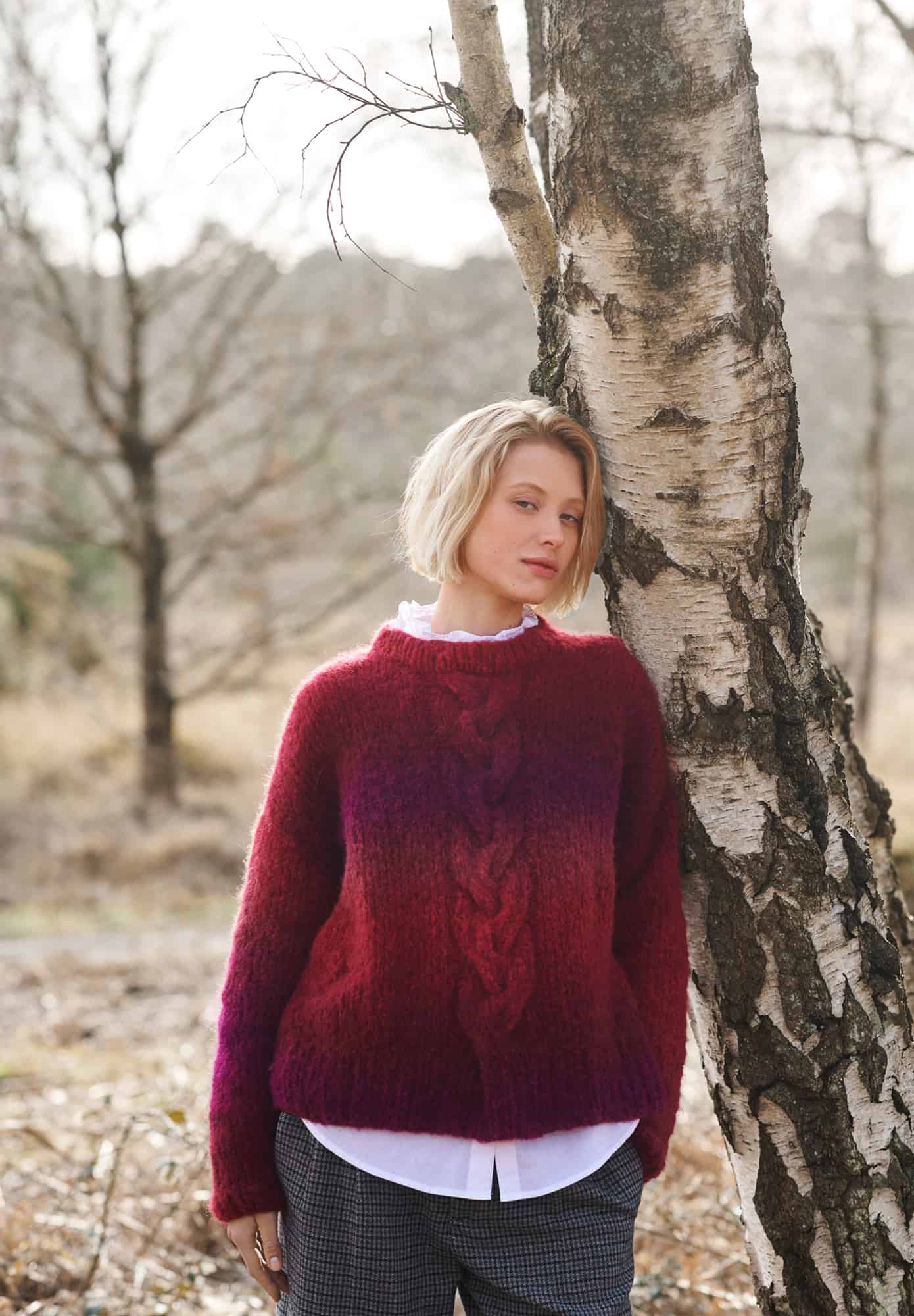 Frau trägt gestrickten Pullover mit Zopfmuster in Beerentönen: Modell 32 aus Lovewool No. 21