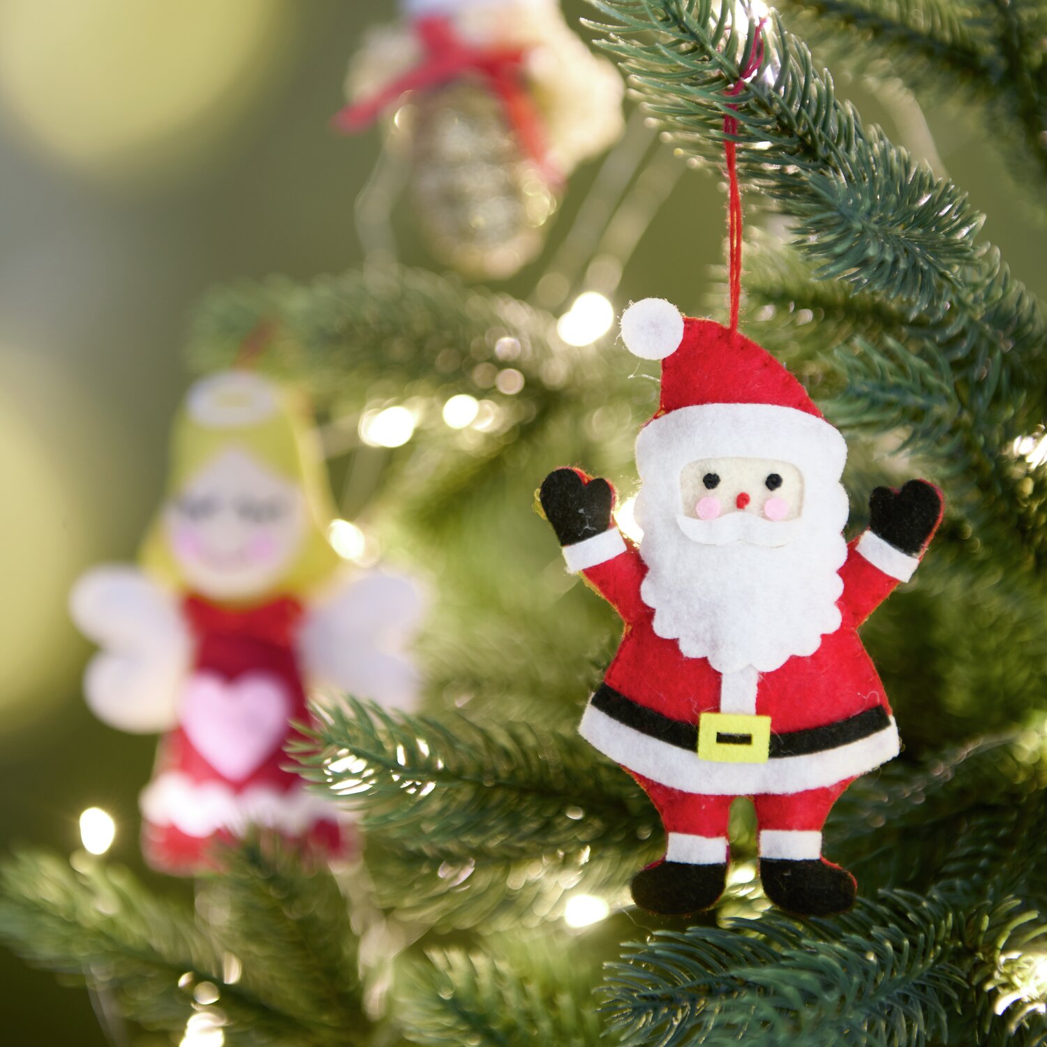 Aufhänger Filz-Weihnachtsmann Rot/Weiß von Rico Design am Weihnachtsbaum, umgeben von Lichtern.