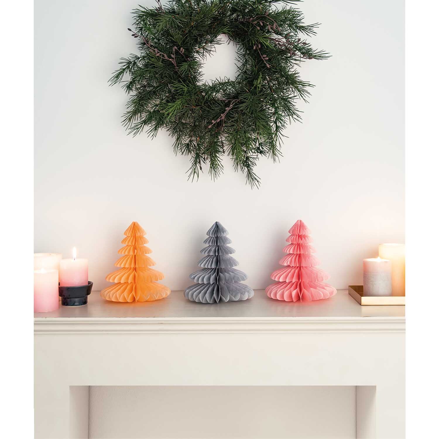 Wabenpapier Tannenbäume 20cm 3 Stück Farbe Pastell von Rico Design Wabenpapier Tannenbäume 20cm 3 Stück in Pastellfarben auf einem Kaminsims, dekoriert mit Kerzen und einem grünen Kranz an der Wand.