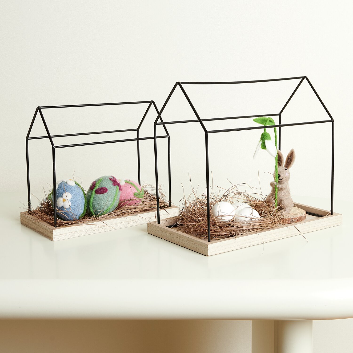 Metall Haus mit Holzboden: Zwei dekorative Metallhäuser mit Holzboden, gefüllt mit Ostereiern und einem Hasen, auf einem Tisch arrangiert.