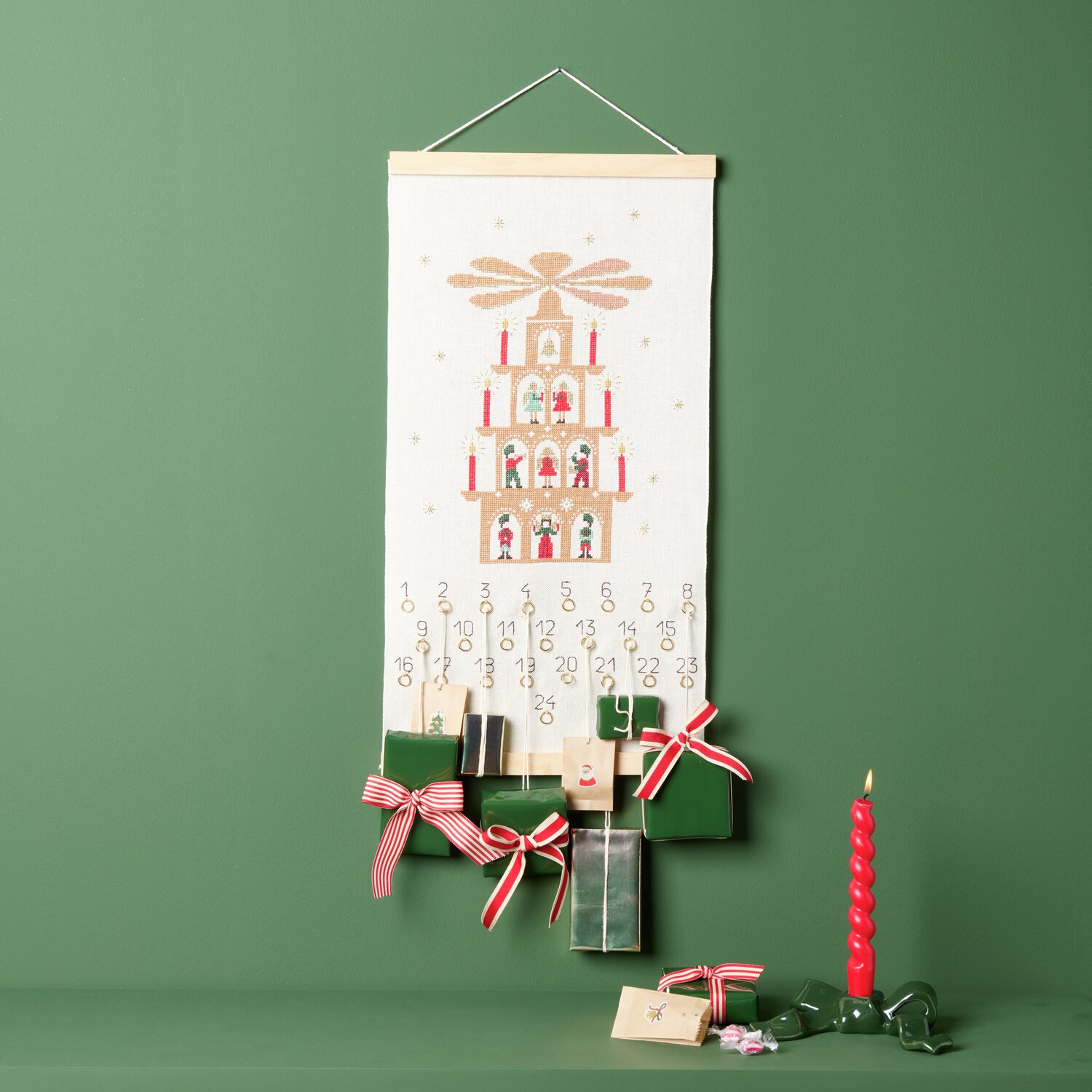 Stickpackung Adventskalender Lichterpyramide 30x56cm von Rico Design Stickpackung Adventskalender Lichterpyramide von Rico Design zeigt eine dekorative Pyramide auf einem grünen Hintergrund mit roten Akzenten.