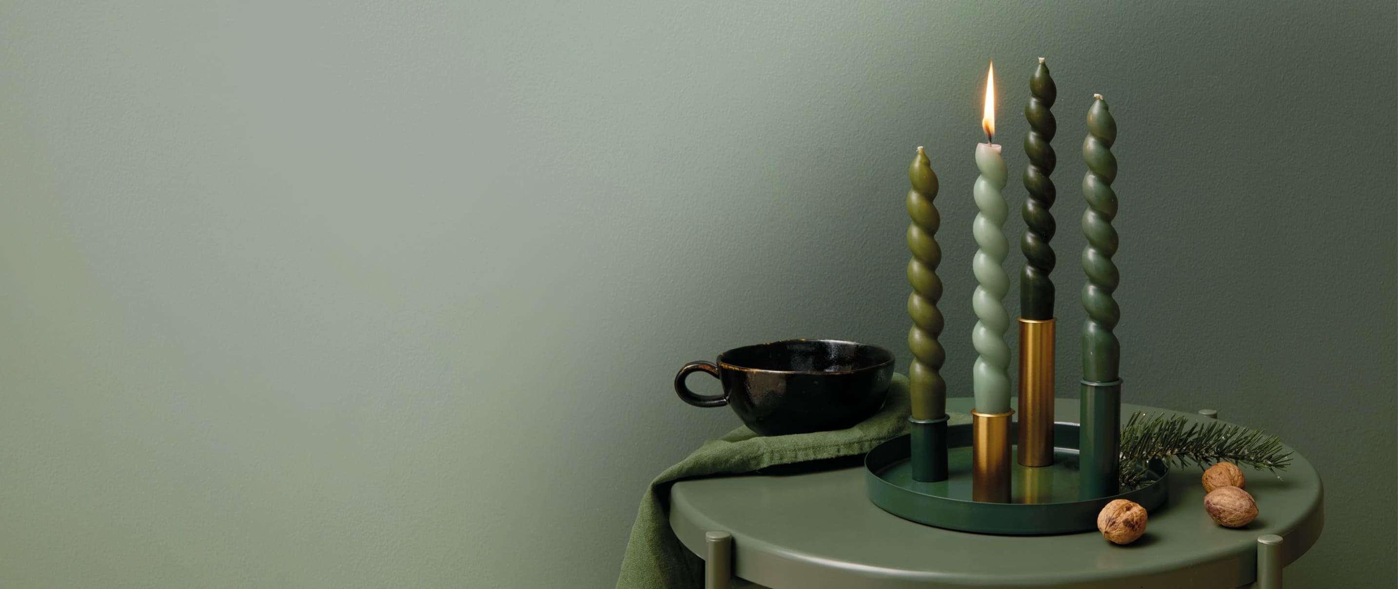 Ein Metalltablett mit Kerzenhaltern ist mit Kerzen in Grüntönen bestückt und weihnachtlich geschmückt.