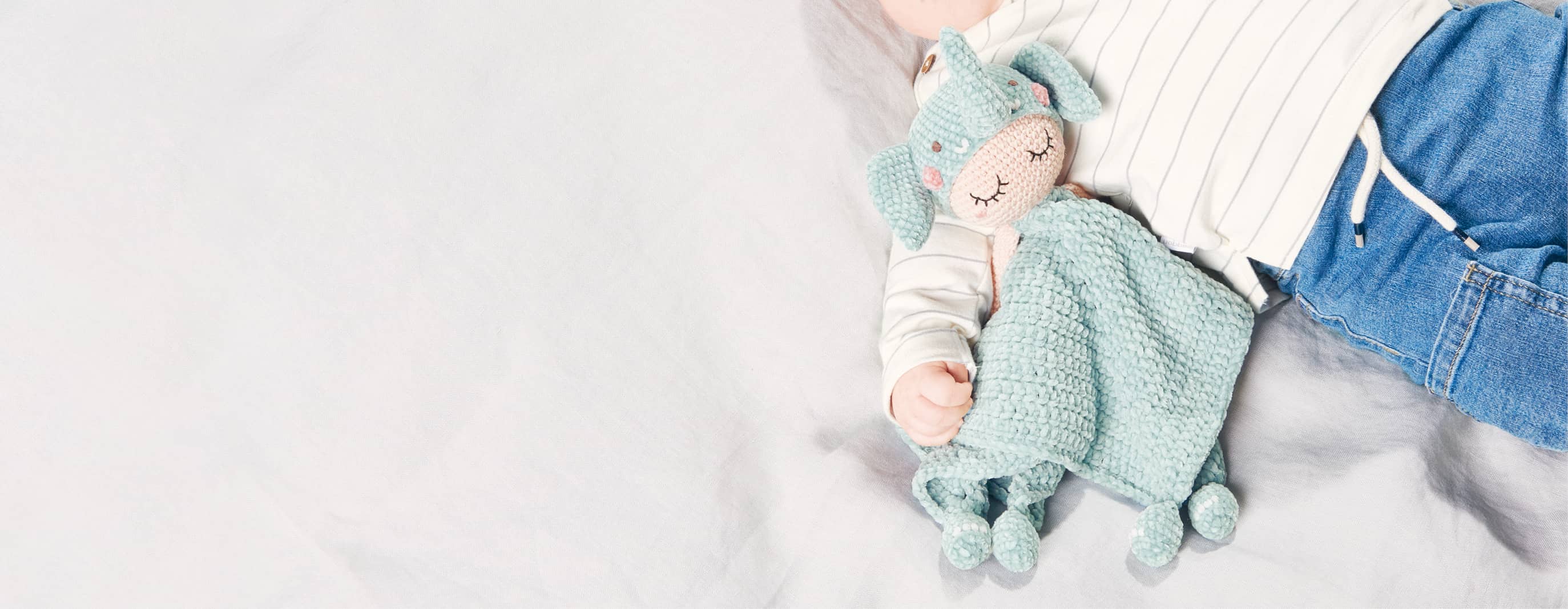 Gehäkeltes Elefanten-Schmustetuch liegt bei Baby im Arm auf einer Decke