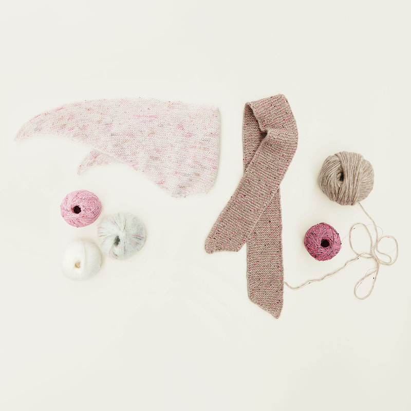 Gestrickte Mini-Tücher liegen zusammen mit Wollknäueln auf hellem Untergrund