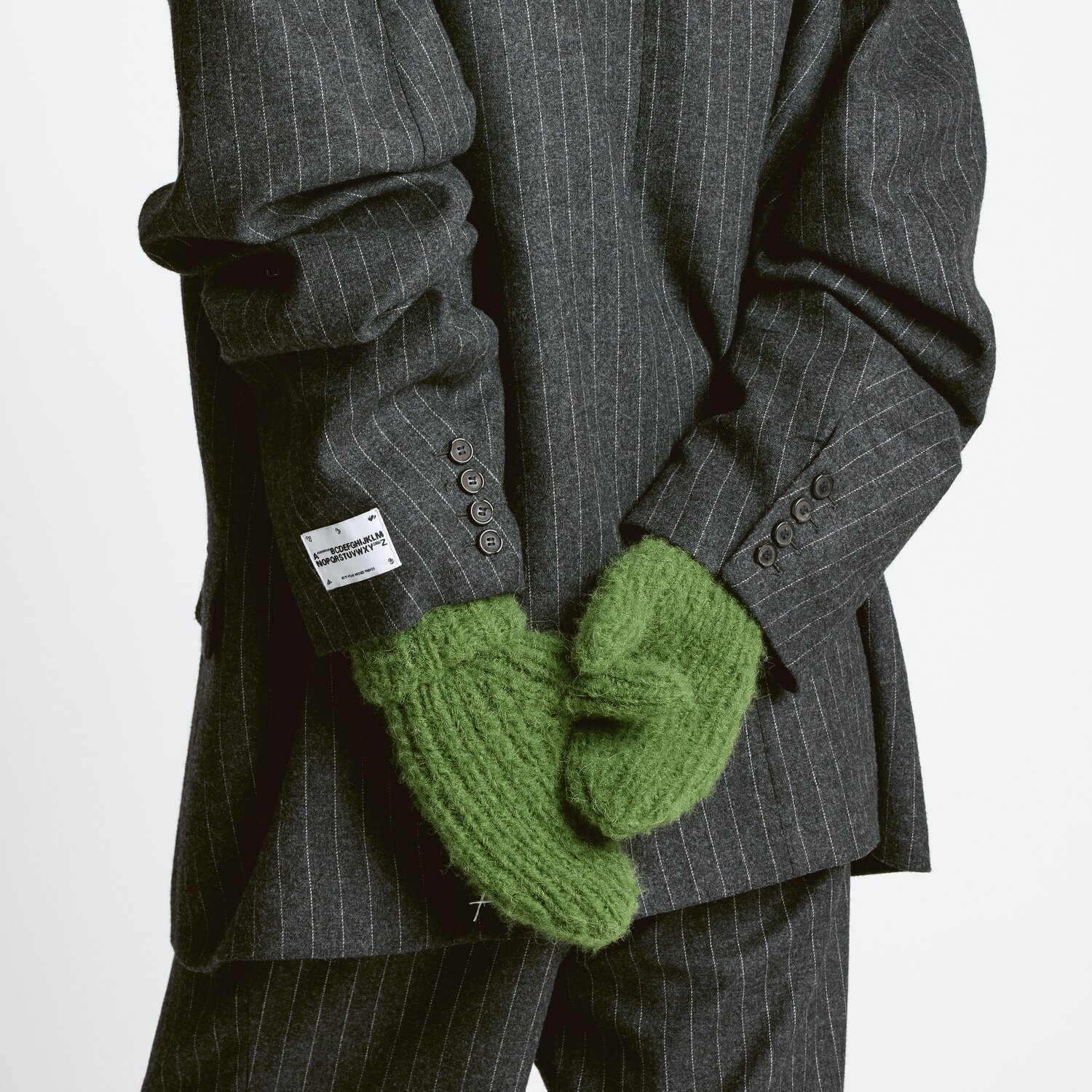 Strickset Handschuhe Modell 20 aus Luxury Knits - Premium Natural Fibres von Rico Design Strickset Handschuhe Modell 20: Grüne Fäustlinge aus Premium Natural Fibres, getragen zu grauem Anzug.