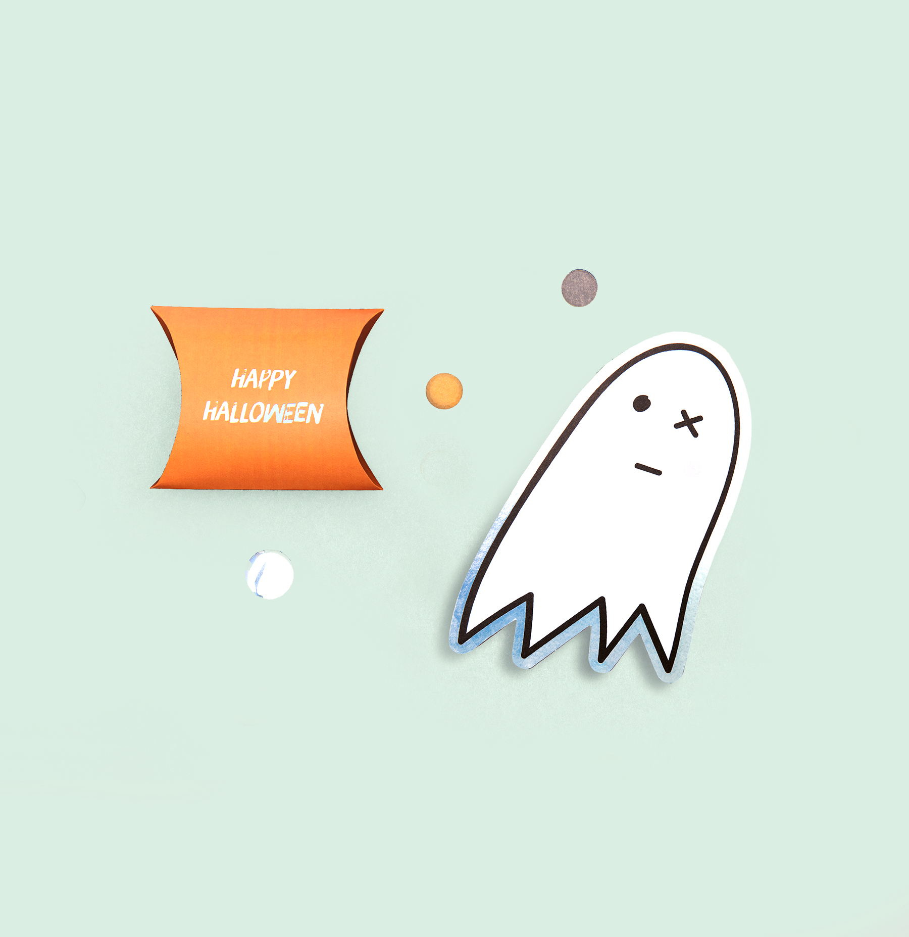 Geschenkschachtel mit Aufschrift Happy Halloween und Sticker in Geisterform liegen auf grünem Hintergrund.