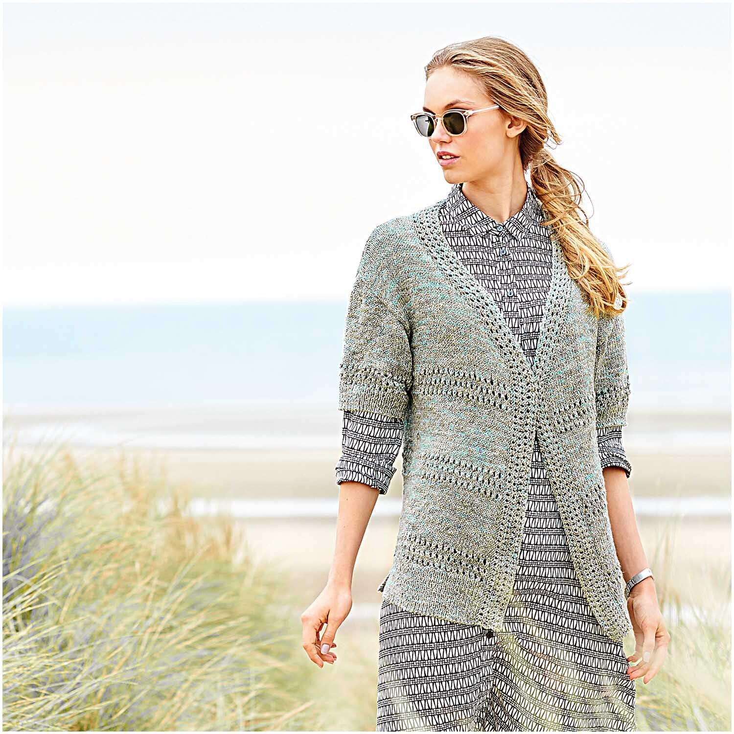 Creative Cotton Zickzack: Frau am Strand in gestricktem Cardigan und Kleid, ideal für kühle Tage.