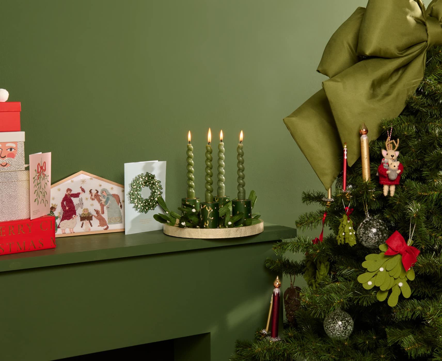 Ein Regal ist weihnachtlich dekoriert mit einem Adventskranz, Weihnachtskarten und Stickbild. Daneben ein geschmückter Weihnachtsbaum.