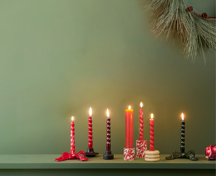 Kerzen und Kerzenhalter in Rot- und Grüntönen sind vor einer grünen Wand dekoriert.
