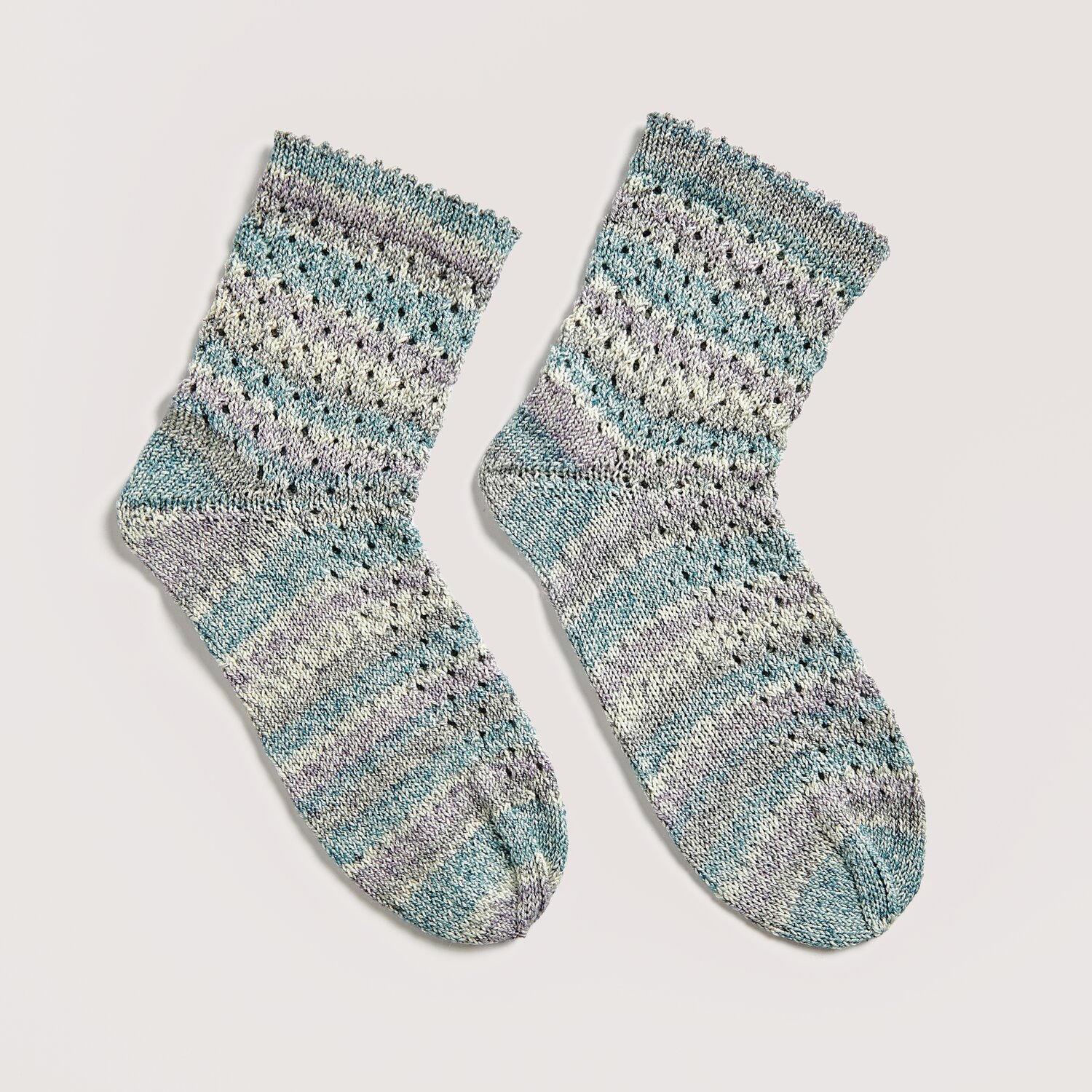 Socks Cotton Stretch 4-fädig 100g 390m Farbe Aqua von Rico Design Strickset Socken Modell 14a aus Die Neue Masche No. 12, gestrickt in Aqua-Tönen, zeigt ein feines Lochmuster. Ideal für Frühling und Sommer.
