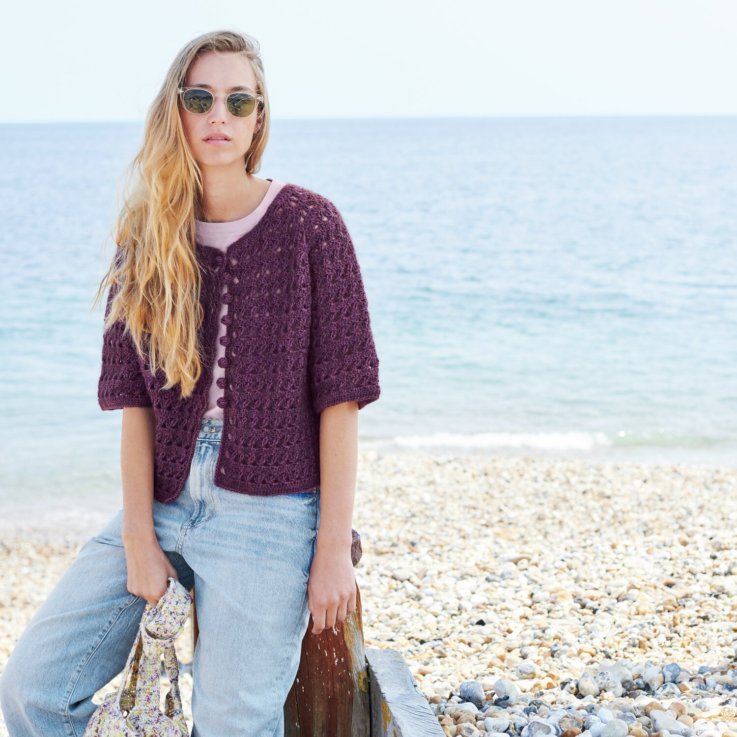 Häkelset kurzarm Jacke Modell 13 B aus Lovewool No. 22 in Lila, getragen von Frau am Strand.