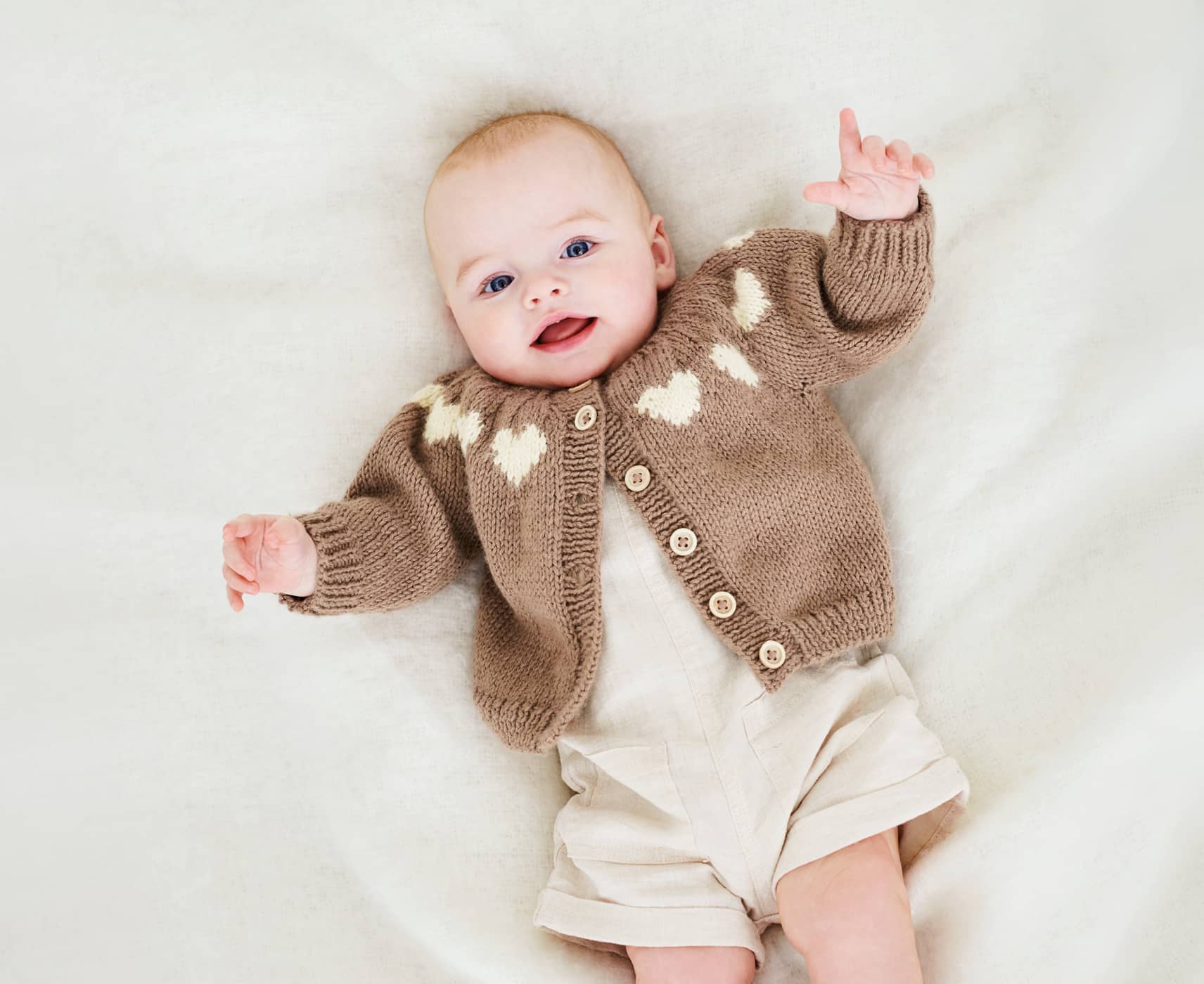 Ein Baby liegt mit einer Strickjacke gekleidet auf einer Decke.