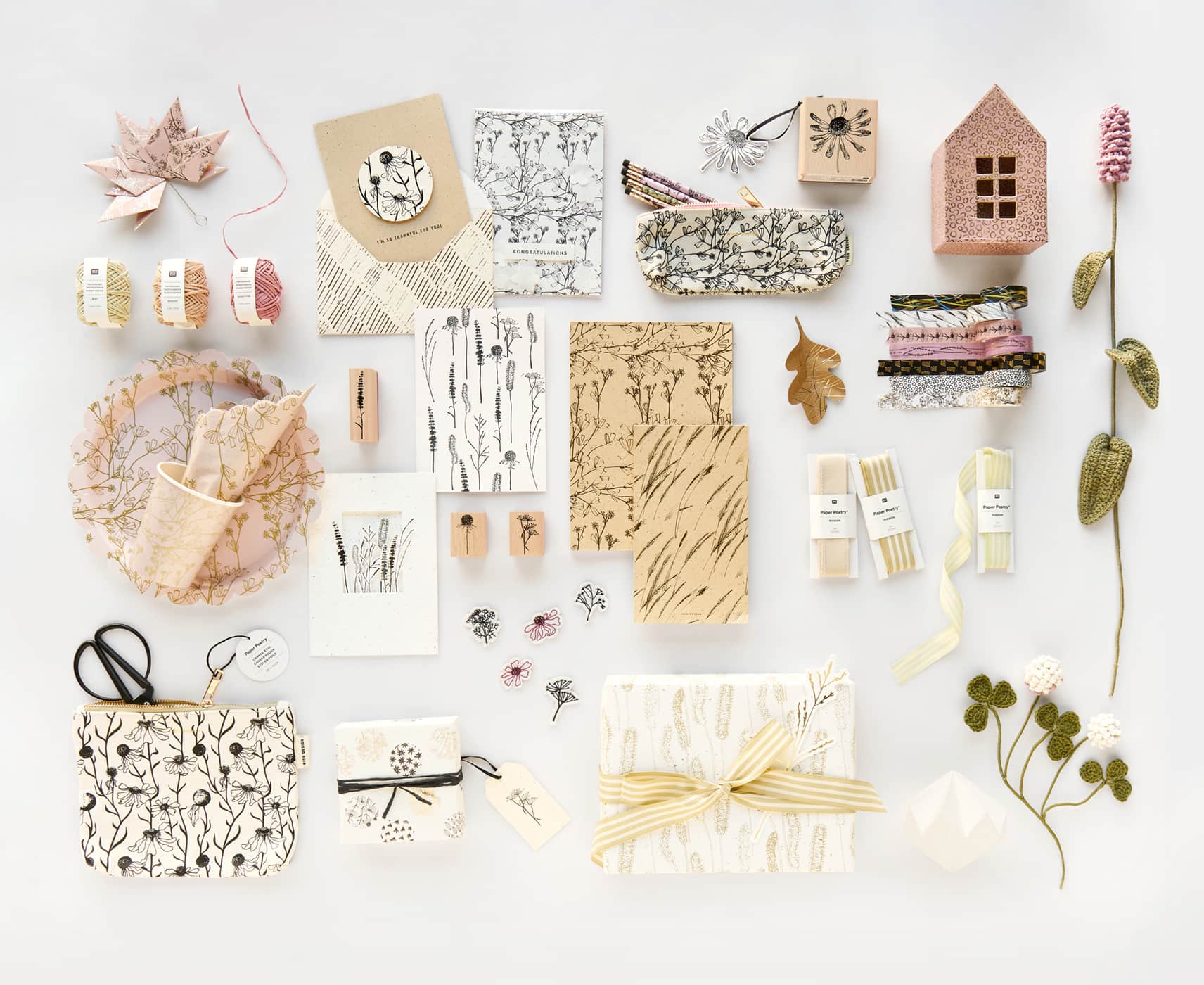 Papierartikel, Etuis, verpackte Geschenke und Pappgeschirr aus der Kollektion "In the Meadow" liegen geordnet auf grauem Hintergrund. 