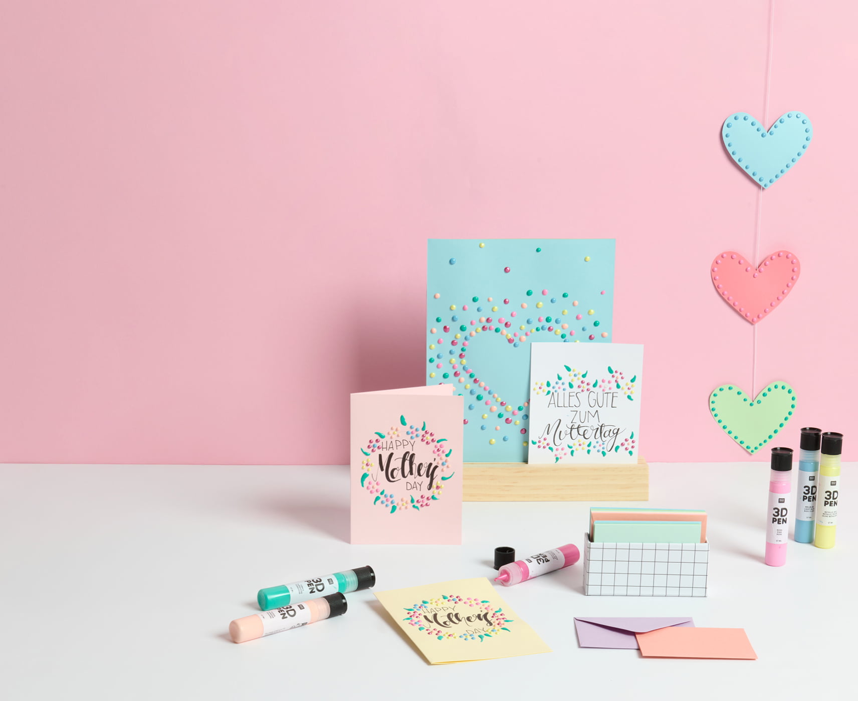 Muttertagskarten sind mit 3D Pens gestaltet und sind vor einer rosa Wand aufgestellt. 3D Pens und Umschläge umgeben die Karten dekorativ.