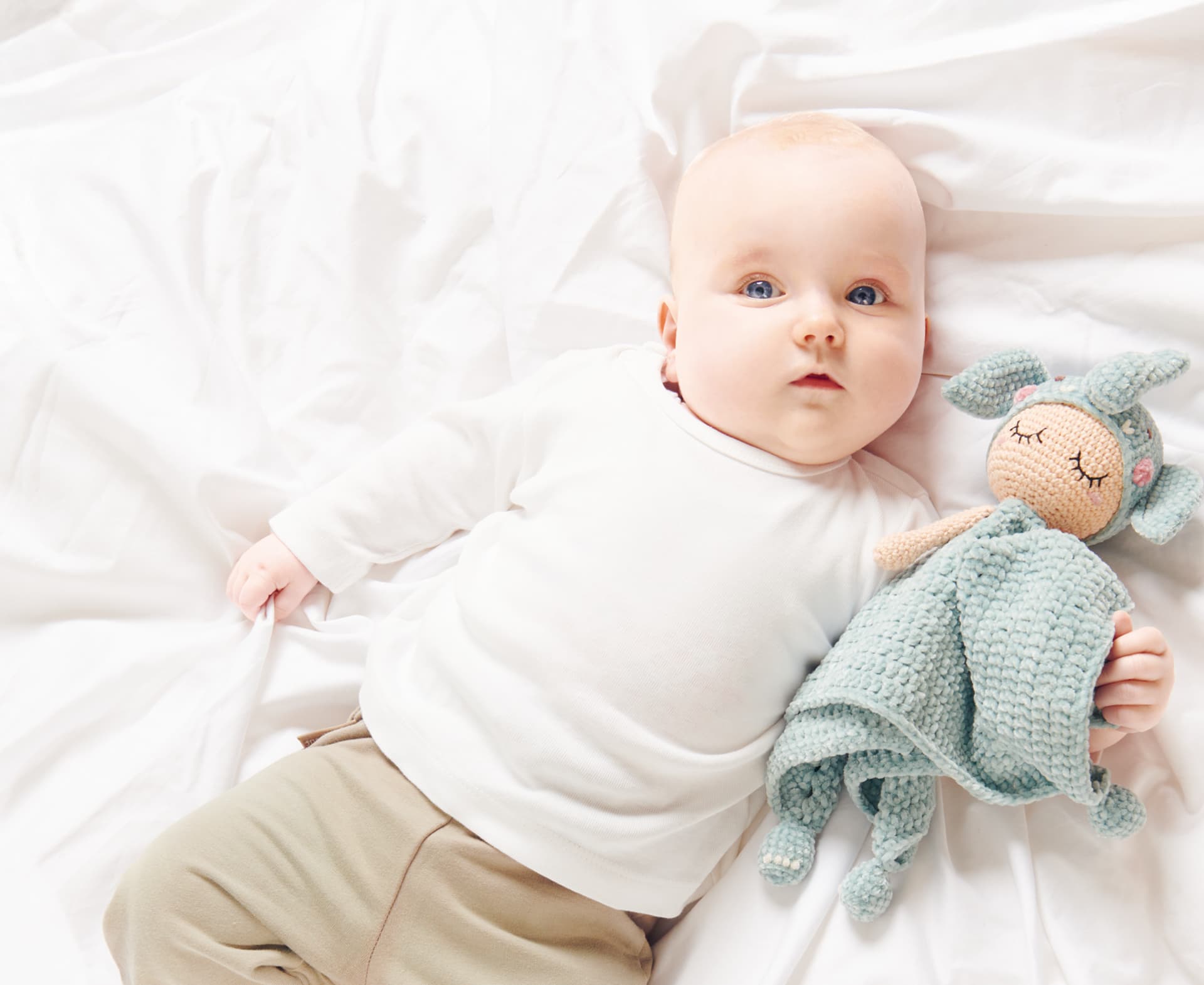 Baby liegt mit gehäkeltem Elefanten-Schmusetuch im Arm auf einer Decke