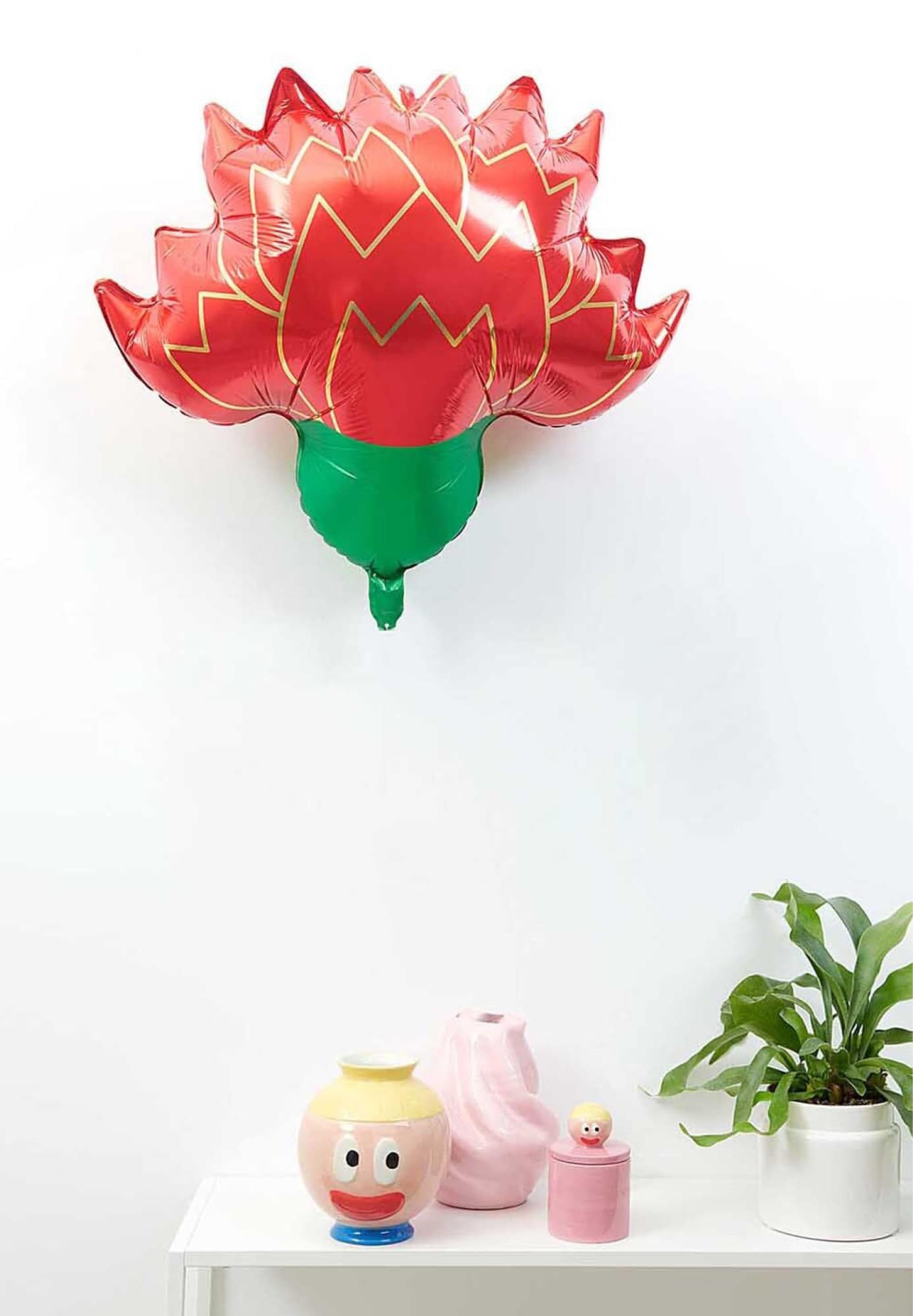 Ein Folienballon in Nelkenform schwebt über einem weißen Tisch mit Dekoration.