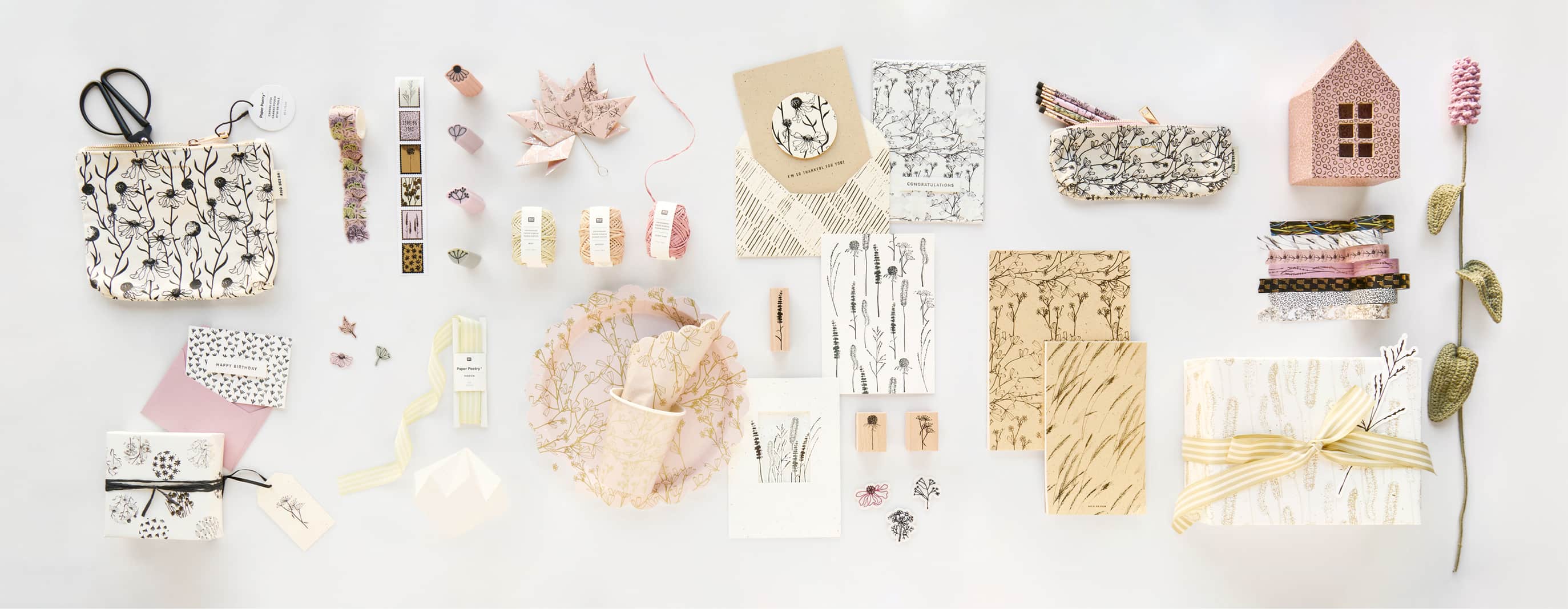 Papierartikel, Etuis, verpackte Geschenke und Pappgeschirr aus der Kollektion "In the Meadow" liegen geordnet auf grauem Hintergrund. 