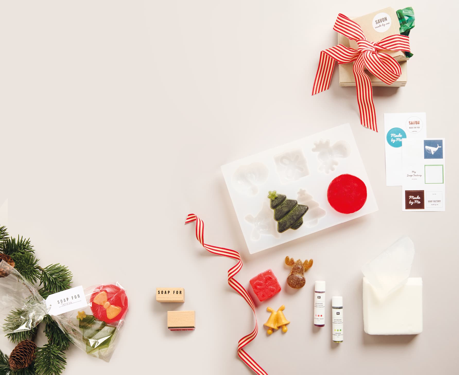 Selbstgemachte Seifen in Weihnachtsformen liegen mit Silikonform, Seifenzubehör und Geschenkverpackungen auf hellem Untergrund.