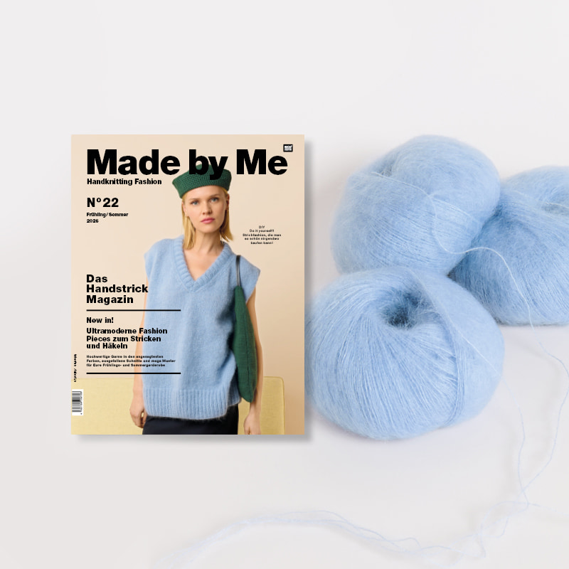 Strickheft Made by Me Nr. 22 neben einem Wollknäuel und Strickstück auf Stricknadeln.