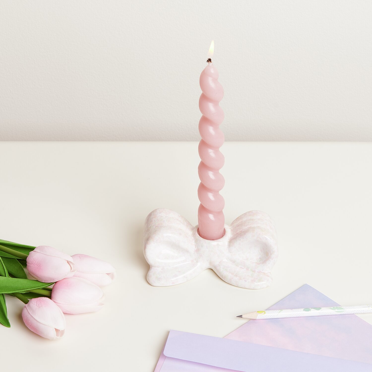 Kerzenhalter Schleife Konfetti: Rosa Kerze in weißem Halter auf Tisch mit Tulpen und Papier.
