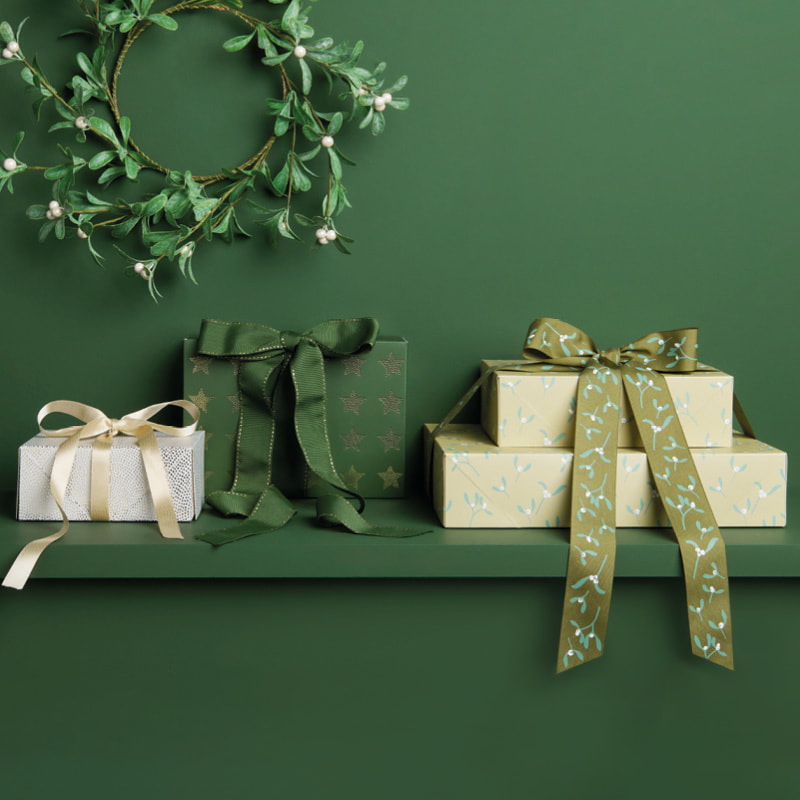 Verpackte Geschenke und Geschenktüten mit weihnachtlichen Designs sind dekorativ vor einem grünen Hintergrund platziert.
