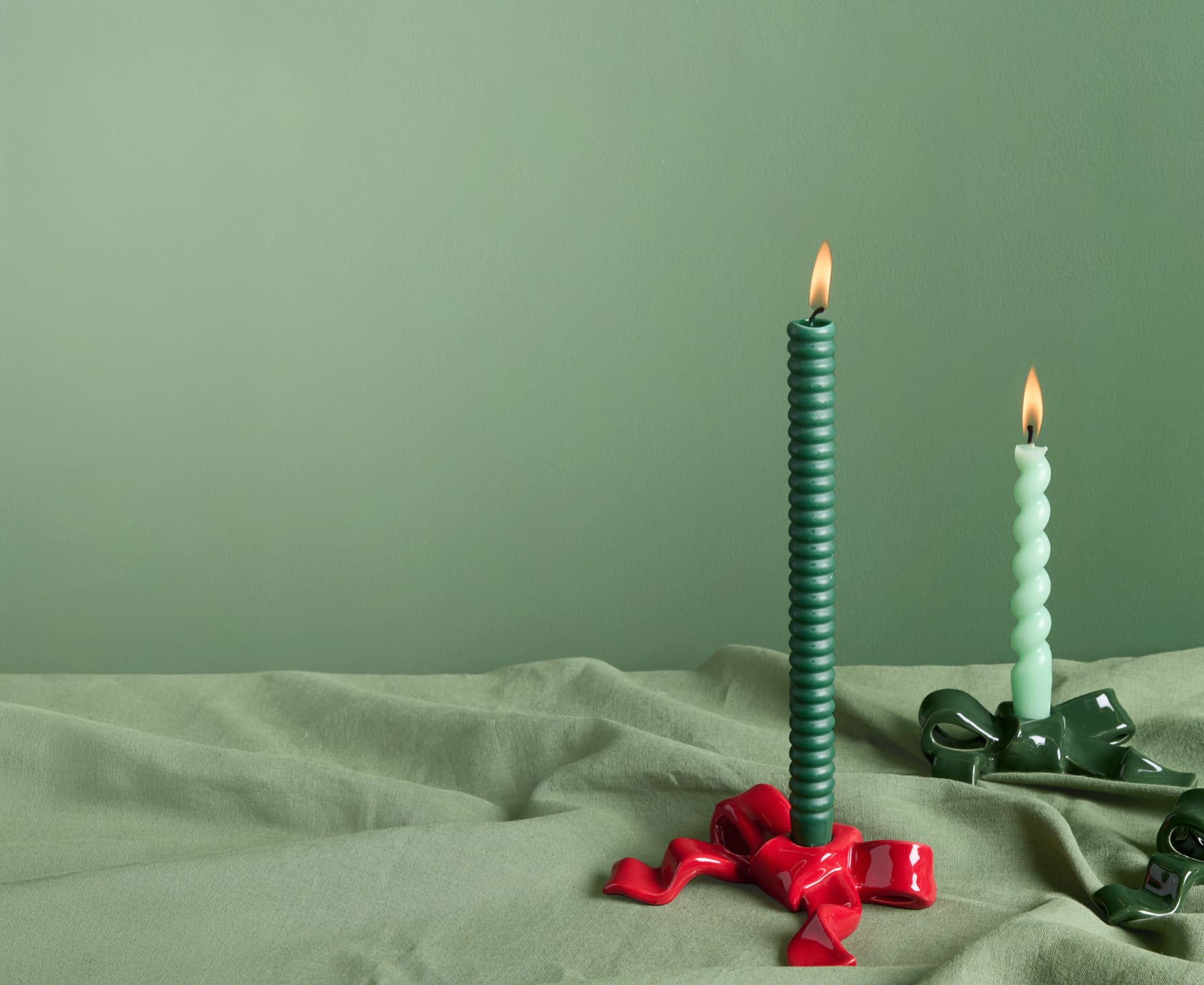 Kerzenhalter Schleife bestückt mit brennenden Kerzen stehen auf grünem Stoff.