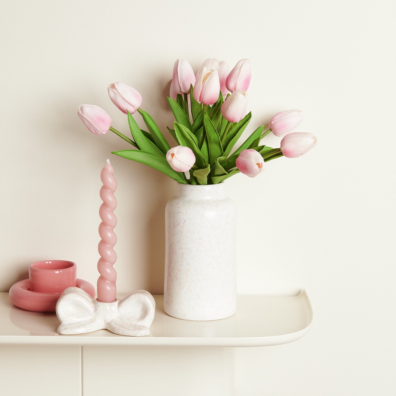 Vase Konfetti mit rosa Tulpen auf einem Tisch, daneben eine rosa Kerze und ein Kerzenhalter.