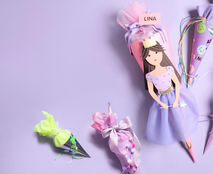 Schultüte mit Prinzessin-Design liegt neben dekorierten Schultüten in kleineren Formaten auf lila Hintergrund