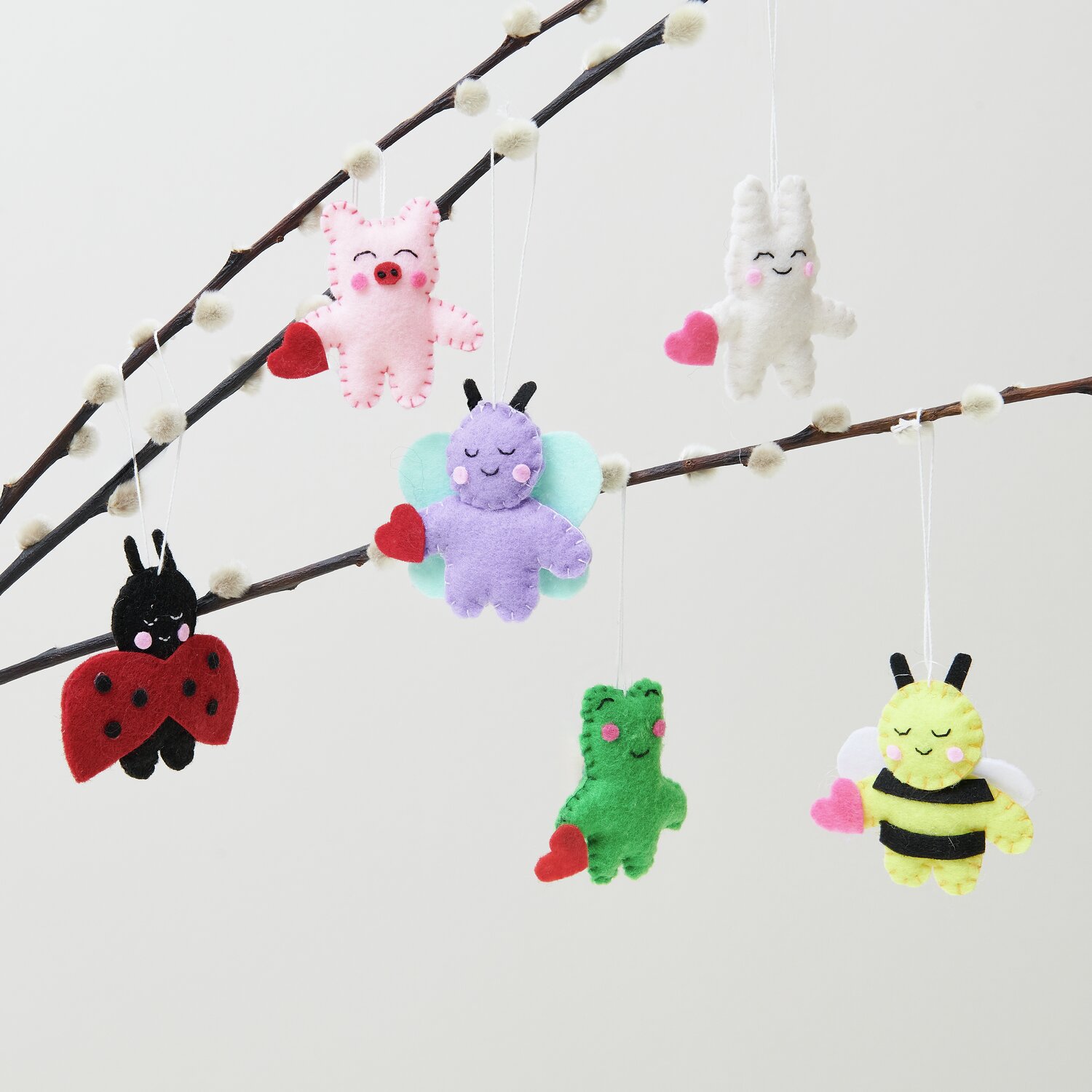 Aufhänger Filz-Hase 2D Weiß: Niedliche Filzfiguren in verschiedenen Farben hängen an einem Ast.