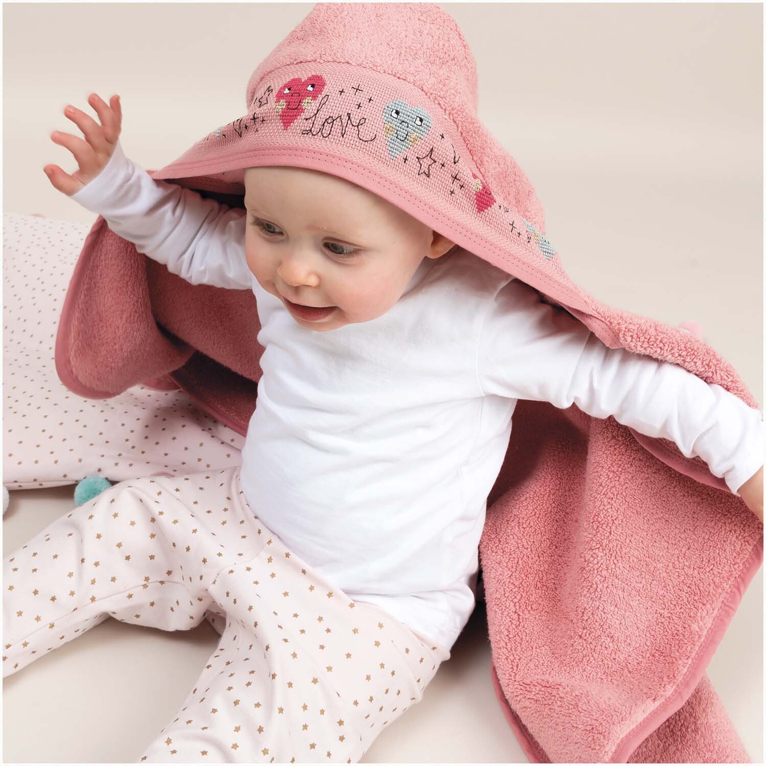 Badetuch mit Kapuze 80x70cm Farbe Hellpink von Rico Design Badetuch mit Kapuze 80x70cm in Hellpink von Rico Design, zeigt ein Baby, das in das weiche Handtuch gehüllt ist.