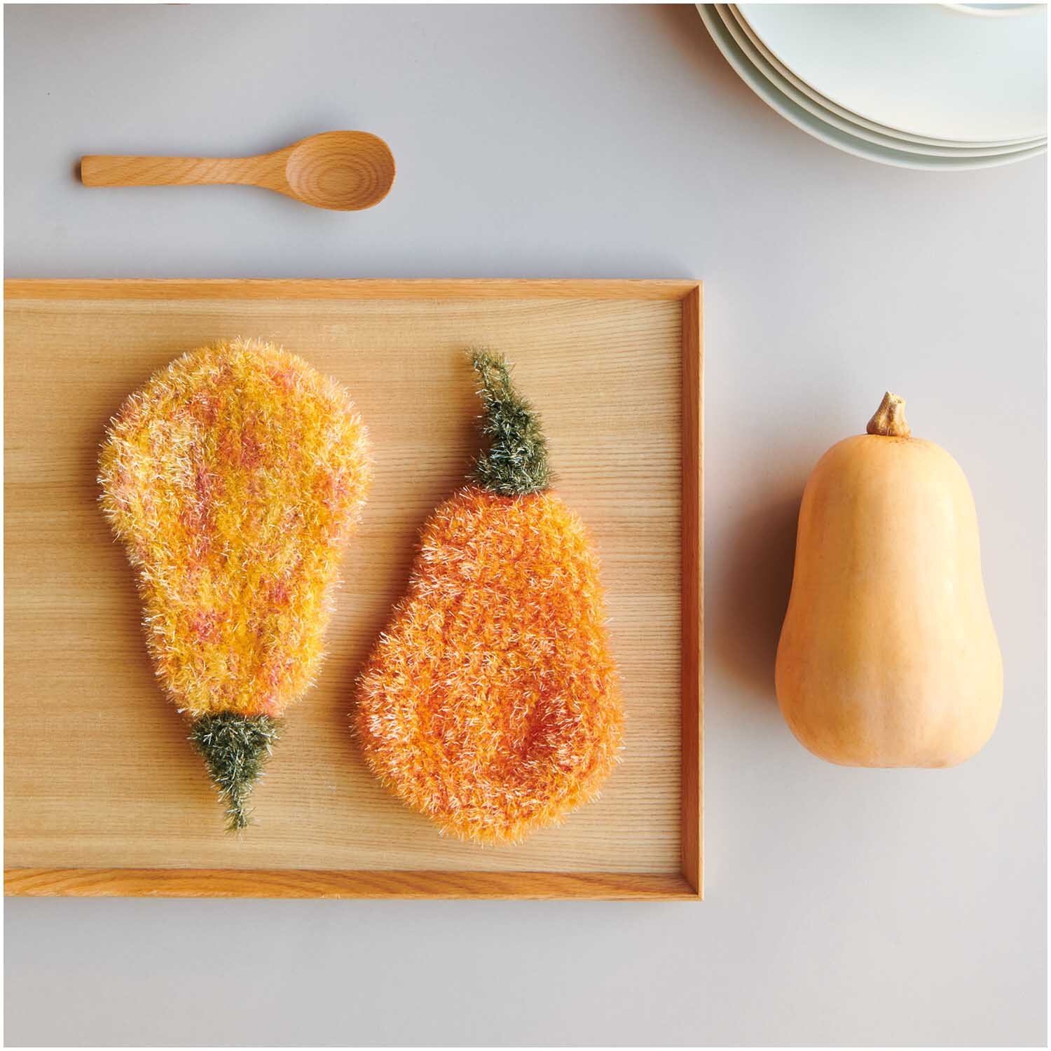 Creative Bubble: Zwei orangefarbene, flauschige Schwämme in Birnenform auf einem Holztablett.