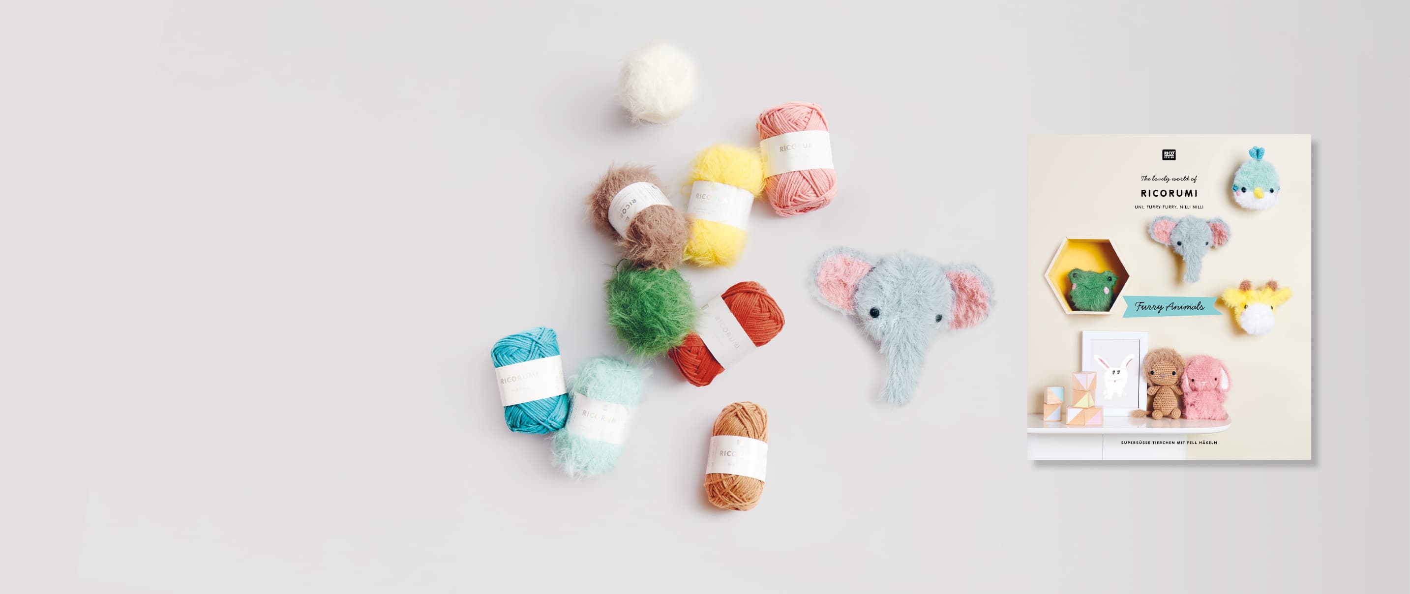 Bunte Knäuel von Ricorumi dk und Ricorumi Furry Furry und ein gehäkelter Elefant liegen verteilt auf grauem Hintergrund. Daneben ein Cover des Häkelhefts Ricorumi Furry Animals.