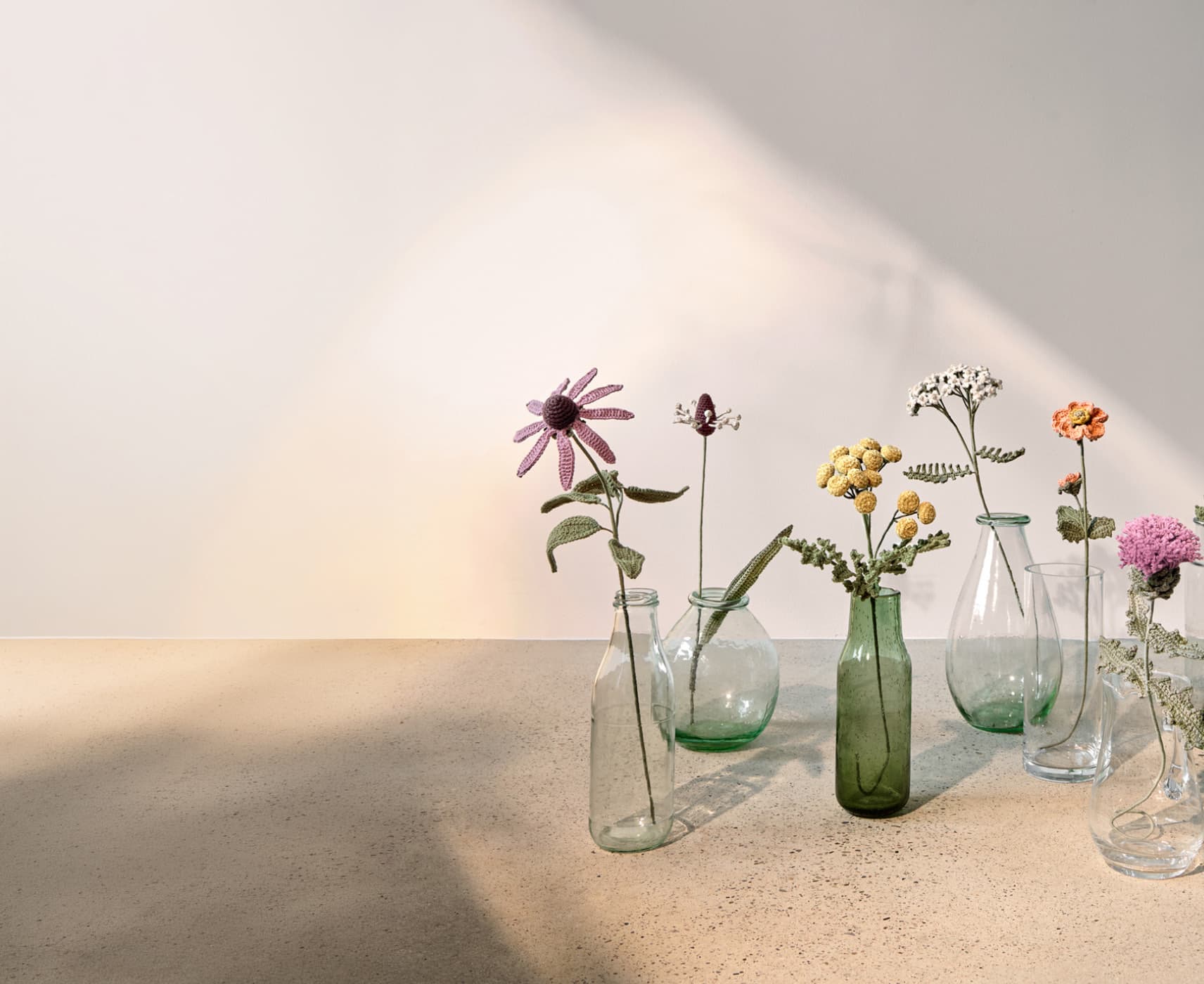 Gehäkelte Wiesenblumen stehen dekorativ in Glasvasen. 