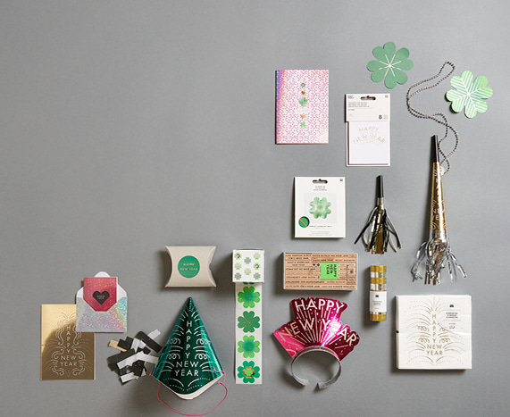 Geschenktüten, Karten, Sticker, Stempel und Party-Accessoires mit Kleeblatt- und "Happy New Year"-Design auf grauem Hintergrund ausgelegt 