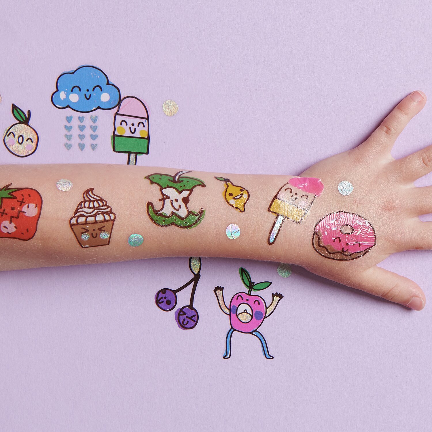 Tattoos Happy Snacks: Bunte, fröhliche Tattoos auf einem Arm, darunter Eis, Donut und Früchte. 23-teiliges Set auf lila Hintergrund.