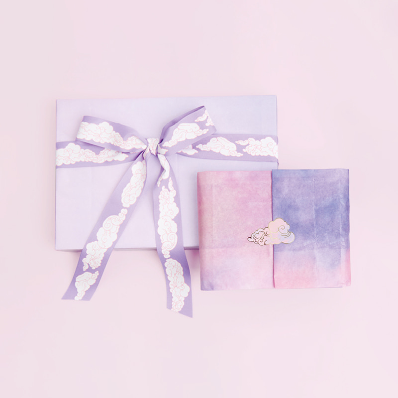 Zwei Geschenke eingeschlagen in Seidenpapier und mit Taftband Wolken verziert, liegen auf rosa Hintergrund.