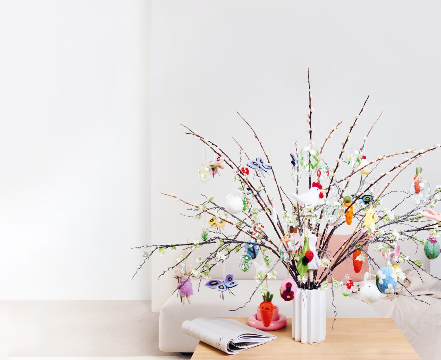 Bunte Anhänger für Ostern und Frühling aus Filz und Glas sind an Zweigen in einer Vase dekoriert. 