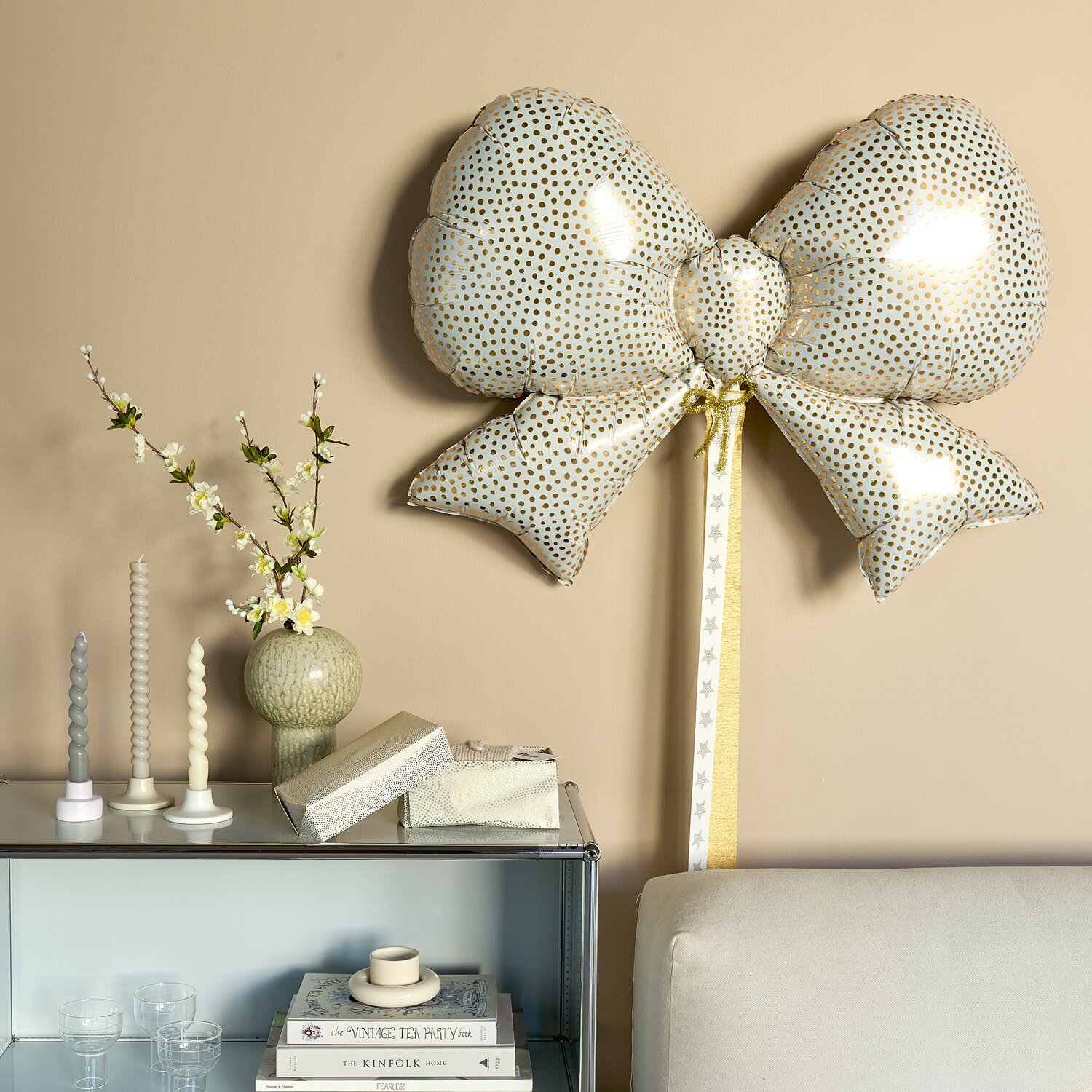 Folienballon Advent Schleife Pünktchen Creme/Gold, festlich dekoriert an Wand, kombiniert mit Porzellan Vase Beige 21x15x15cm und stilvoll arrangierten Kerzen.
