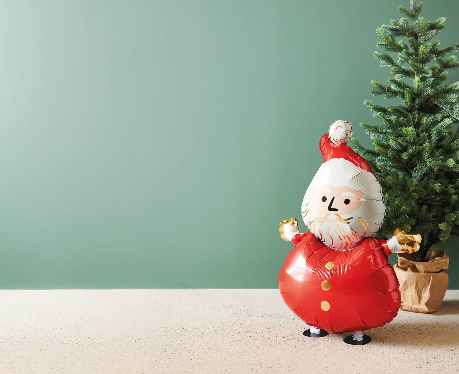 Folienballon in Form eines Weihnachtsmanns vor grünem Hintergrund und Tannenbaum