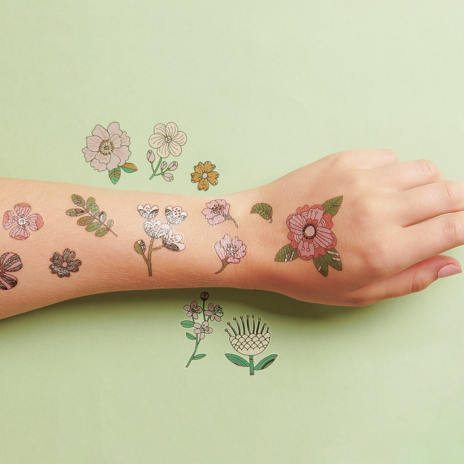 Tattoos Hygge Blumen: Temporäre Blumen-Tattoos auf einer Hand, 16-teilig, auf grünem Hintergrund.