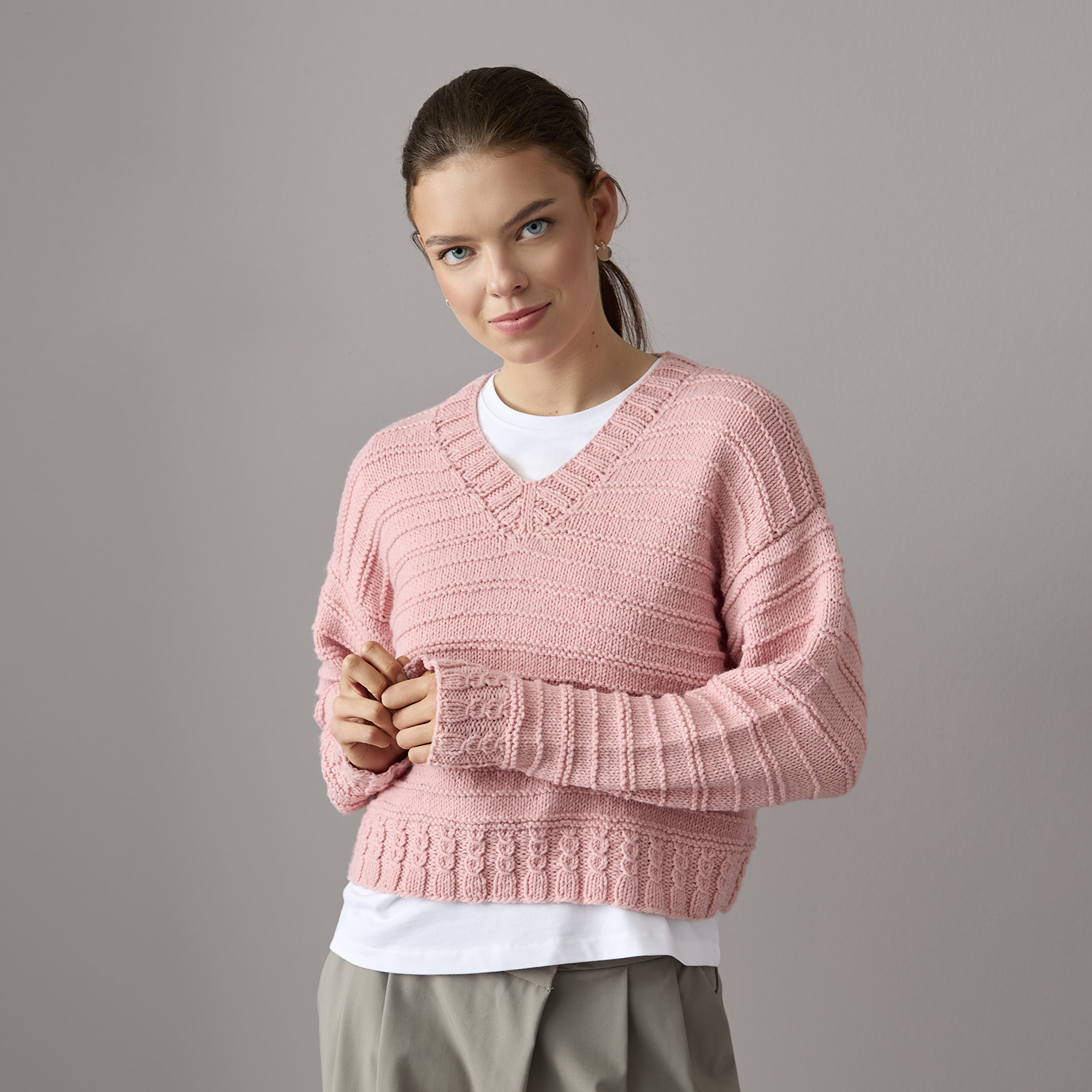 Strickanleitung Pullover aus Essentials Vegan Cashmere aran: Rosa V-Pullover, lässig gestylt über weißem Shirt, ideal für kühle Tage.