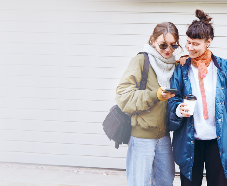Zwei Frauen stehen beieinander und tragen gestrickte Halstücher. Daneben ein Cover des Strickhefts Mini Tücher Special.