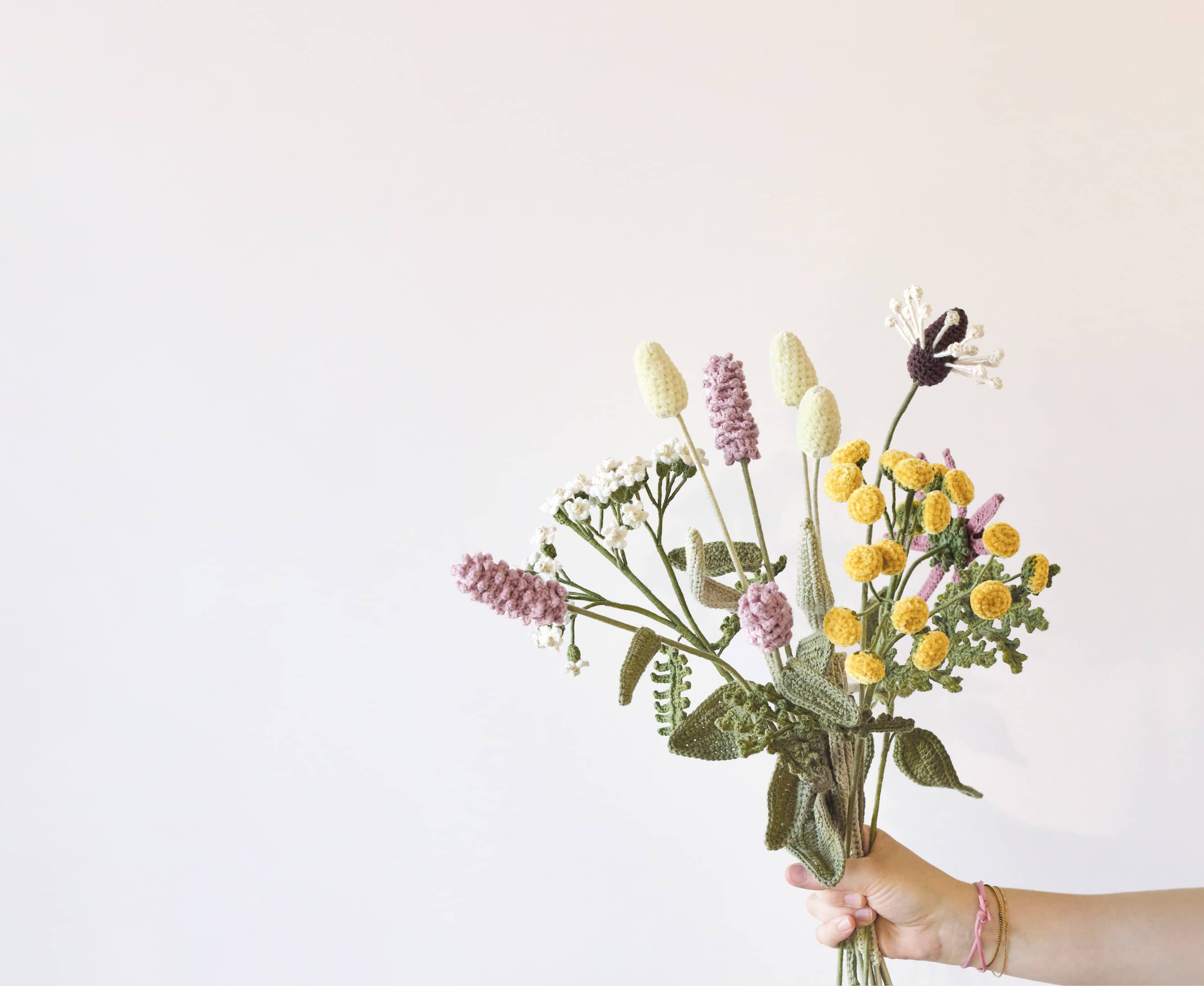 Eine Hand hält gehäkelte Wildblumen, die zu einem Blumenstrauß arrangiert sind.