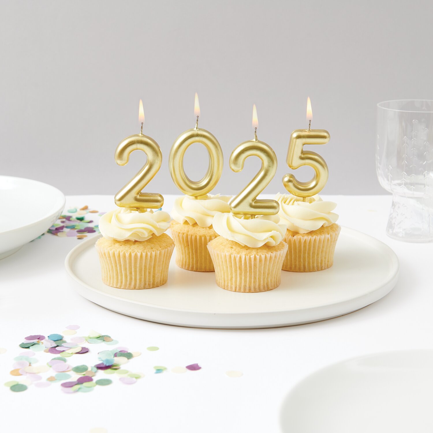 Zahlenkerze Gold von Rico Design, brennende Kerzen in Form der Jahreszahl 2025 dekorieren vier festliche Cupcakes auf einem hellen Partytisch
