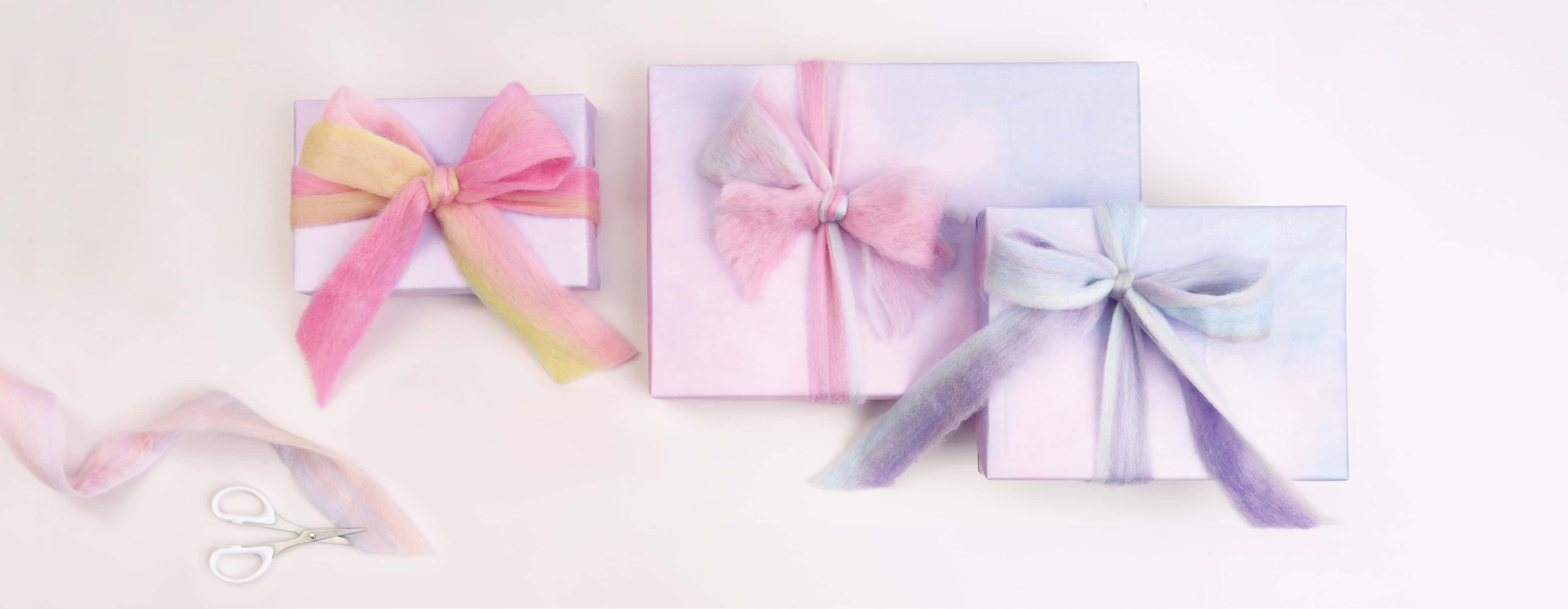 Verpackte Geschenke in Pastelltönen sind mit Filzband geschmückt. 