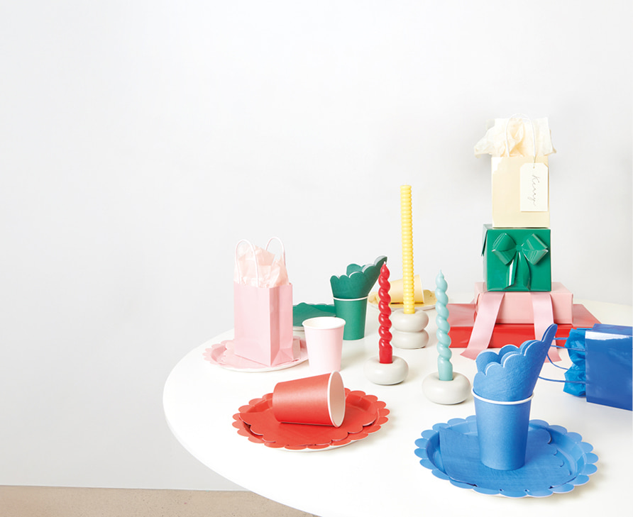 Gedeckter Tisch mit farblich abgestimmten Party-Sets aus Servietten, Tellern und Bechern in rot, grün, blau und lila