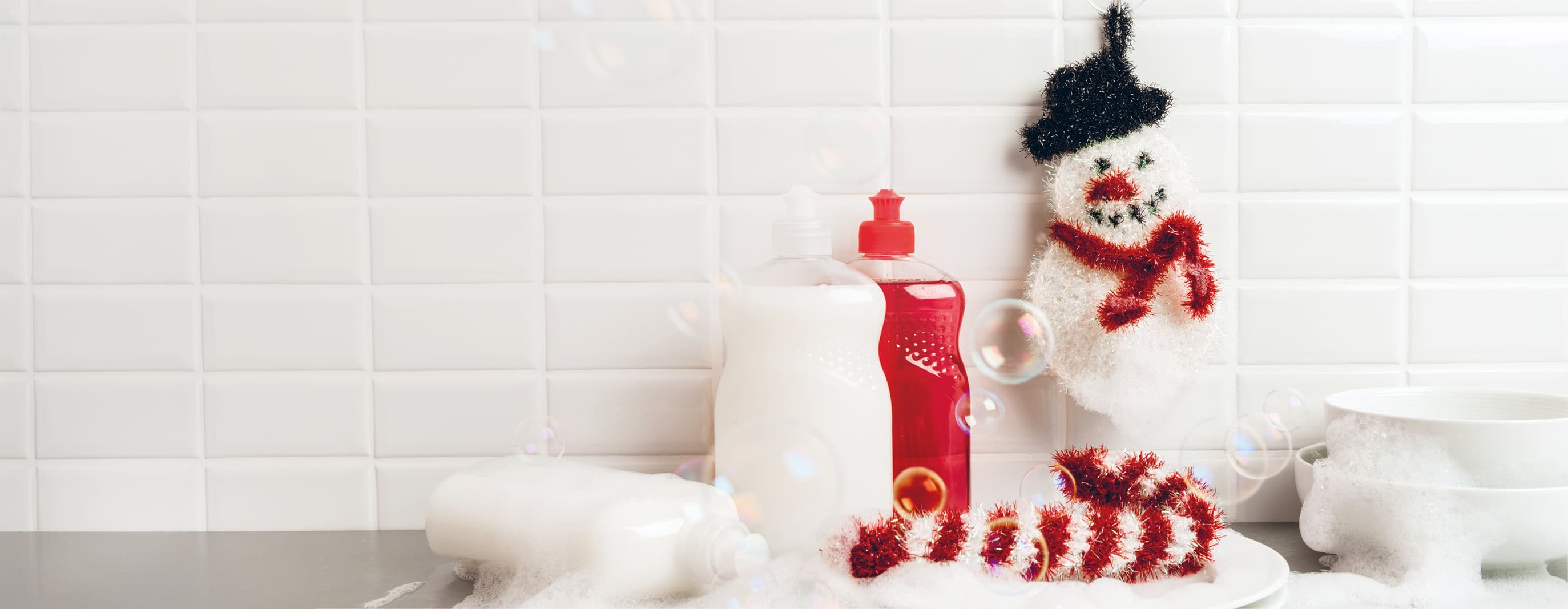 Gehäkelte Spülschwämme in Form von Schneemann und Zuckerstange sind an einem Spülbecken dekoriert