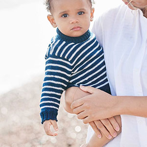 Baby trägt gestreiften Strickpulli auf dem Arm seiner Mama